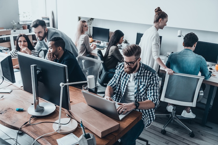 Concentrated at work. Group of young beautiful people using computers and communicating while working in office together